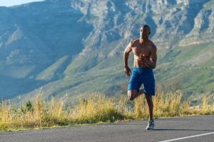 Athletic, sporty, muscular, healthy black male running along a road outdoors with a mountain background.