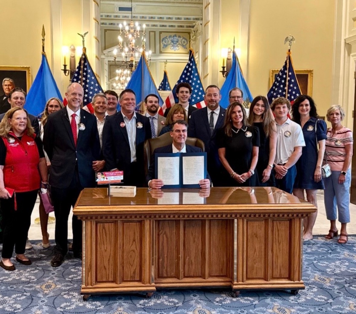 group of advocates gathered around Governor Kevin Stitt's desk for bill signing