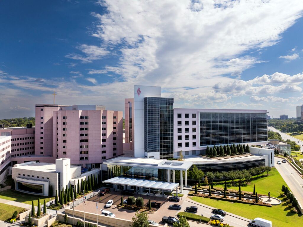Aerial view of Saint Francis Hospital in Tulsa, Oklahoma, showing the hospital campus with multiple medical buildings, a glass-front patient tower, landscaped grounds, and the main entrance.