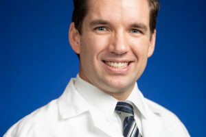 Dr. Jordan Schaefer, hematologist at University of Michigan Health, wearing a white lab coat with the University of Michigan logo.