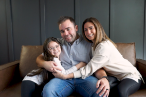 young family of three sitting on brown couch and hugging