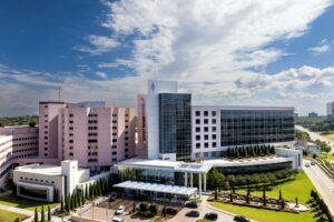 Aerial view of Saint Francis Hospital in Tulsa, Oklahoma, showing the hospital campus with multiple medical buildings, a glass-front patient tower, landscaped grounds, and the main entrance.